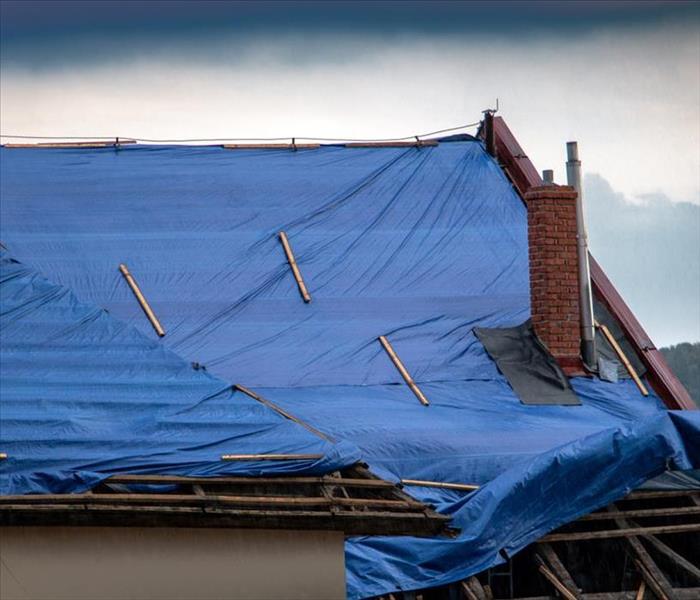 The protective tarpaulin on the roof flutters at the storm with rain. The tarp covers the roof of the old house in the recons